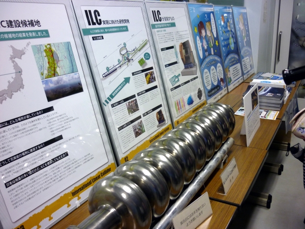 A superconducting radio frequency cavity that will be used in the ILC, on display with some posters